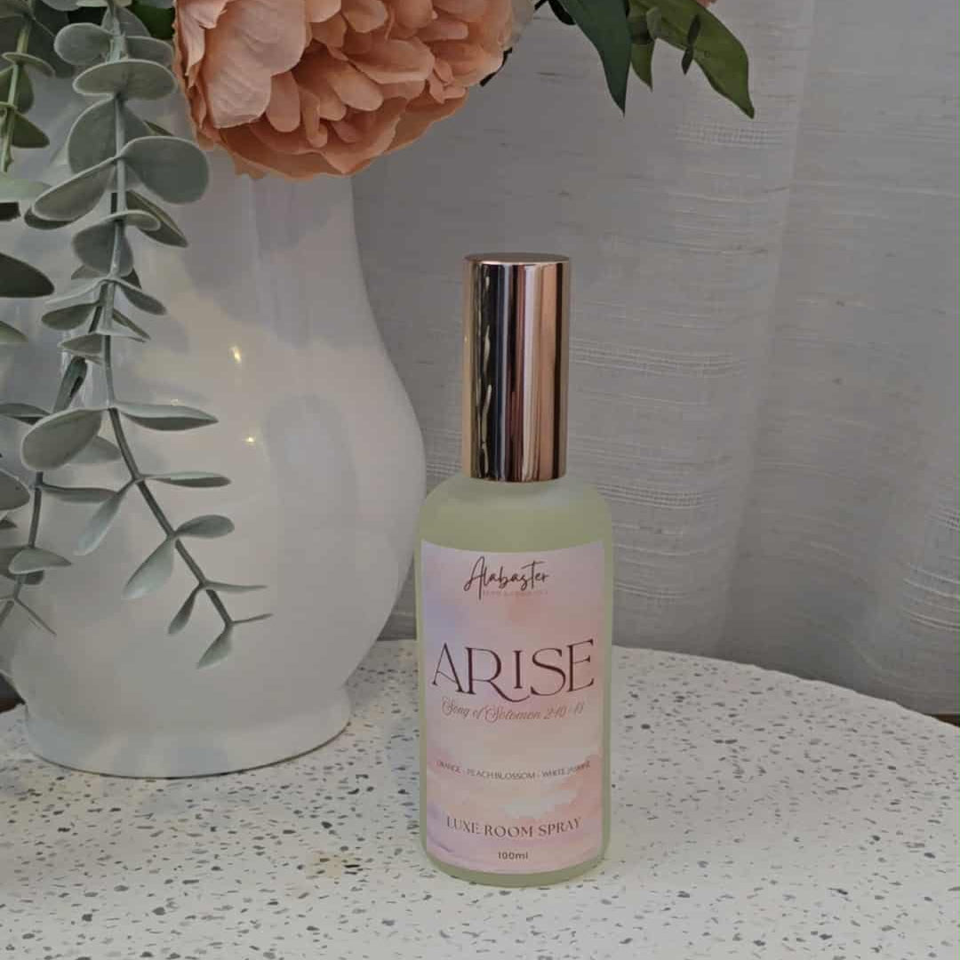 Bottle of 'Arise' on a textured surface with flowers in the background