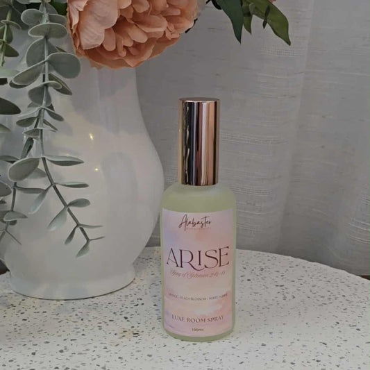 Bottle of 'Arise' on a textured surface with flowers in the background